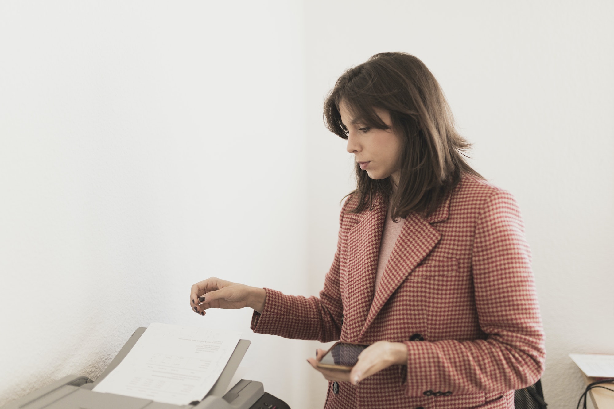Serious woman with smartphone near documents on printer
